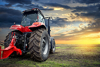 Roter Traktor auf Wiese vor Sonnenuntergang.