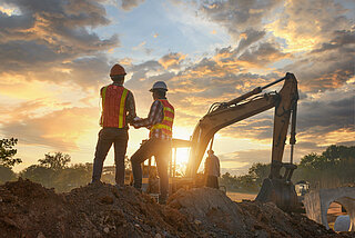 Imagem representativa no canteiro de obras com escavadeira e dois trabalhadores